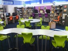 an empty library filled with lots of green and white tables, chairs and bookshelves