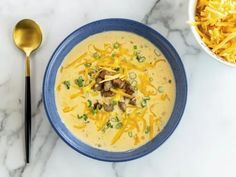 a bowl of cheese soup next to a spoon on a marble counter top with shredded cheese