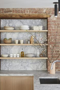 a kitchen with brick walls and open shelving above the sink is featured in this article