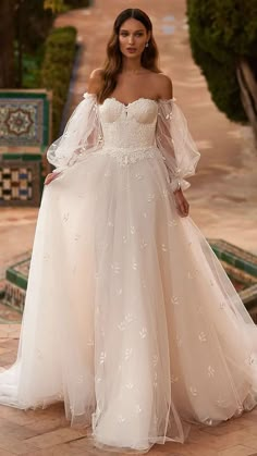 a woman in a white wedding dress standing on a stone walkway with trees and bushes behind her