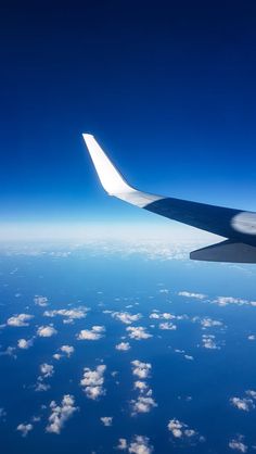 the wing of an airplane flying in the sky above clouds and land below it is blue with white fluffy clouds