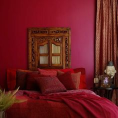 a bed with red sheets and pillows in front of a wooden headboard against a pink wall