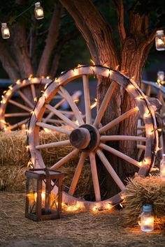 an old wagon wheel is surrounded by candles and mason jar lights in front of a tree