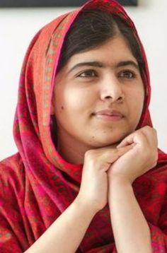 a woman wearing a red and pink shawl with her hands on her chest looking at the camera