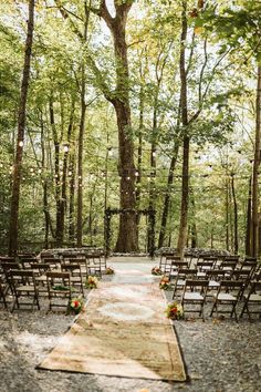 an outdoor ceremony setup with wooden chairs and flowers on the aisle, surrounded by trees