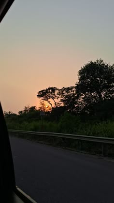 the sun is setting behind some trees on the side of the road as seen from inside a car