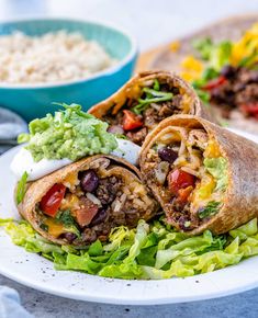 two burritos on a plate with lettuce, tomatoes and black beans