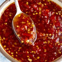 a spoon full of chili sauce with corn on the cob and some seasoning