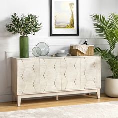 a white sideboard sitting next to a potted plant