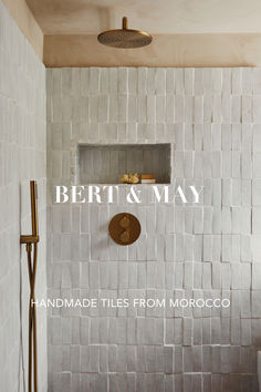 a bathroom with white tiles and gold fixtures on the shower head is featured in an ad for bert & may