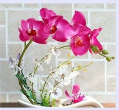 pink flowers are in a white vase on a wooden table next to a brick wall