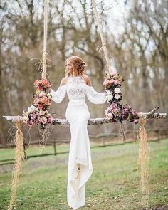 a woman is sitting on a swing with flowers in her hair and wearing a white dress