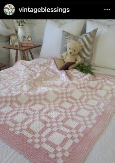 a teddy bear sitting on top of a bed with pink and white quilts in it