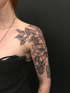 a woman wearing a black dress with flowers on her arm and shoulder, in front of a dark background