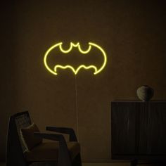 a neon batman sign is lit up in the dark room with a chair next to it