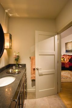 a bathroom with a sink, mirror and door leading to a bed in the background