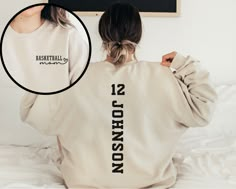 a woman sitting on top of a bed wearing a white sweatshirt with the words basketball season written on it