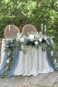 the table is set with blue and white flowers, greenery and candles on it