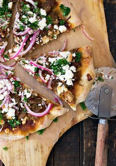 a pizza with onions, cheese and herbs on a cutting board next to a spatula