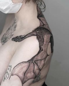 a woman wearing a face mask with a dragon tattoo on her chest and shoulder,