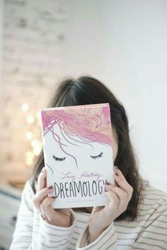 a woman holding up a book in front of her face with the words dream on it