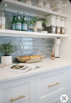 a kitchen with white cupboards and shelves filled with bottles, dishes, and other items