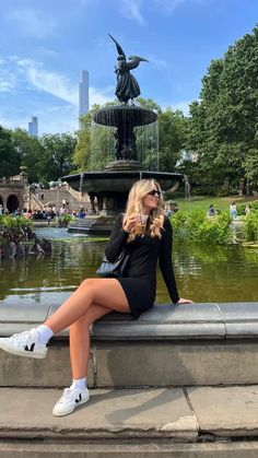 a woman sitting on the edge of a fountain taking a selfie