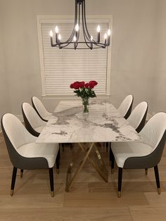 a marble dining table with six chairs and a vase of roses on the end, in front of a chandelier