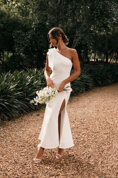 a woman in a white dress holding a bouquet and posing for the camera with her legs slited