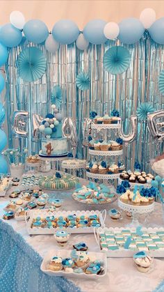 a table topped with lots of desserts next to blue and white balloons in the air