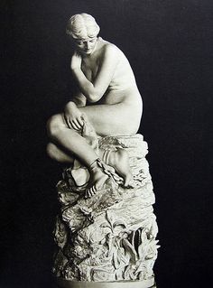 a black and white photo of a nude woman sitting on a pile of cloths