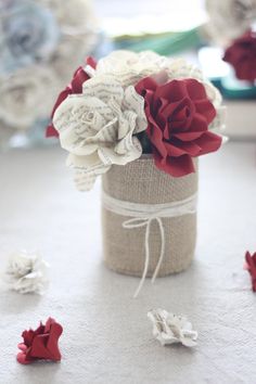 some red and white flowers in a vase on a table with other items around it