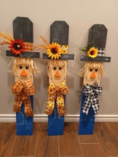 three scarecrows with sunflowers on their heads are standing in front of a wall