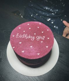 a pink birthday cake sitting on top of a white plate next to a person's hand