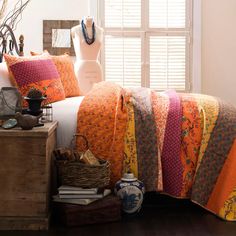 a bed covered in an orange quilt next to a window