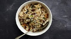 a white bowl filled with rice and meat on top of a black table next to a spoon