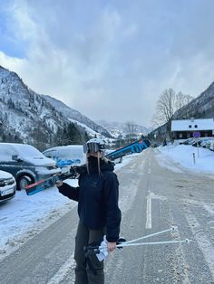 a man standing on the side of a snow covered road holding skis and poles