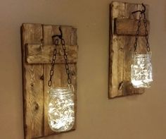 two mason jars are hanging on the wall with chains attached to them, and one is lit up