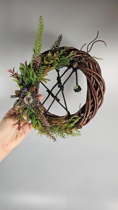 a hand holding a wreath with plants in it