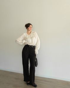 a woman standing in front of a white wall with her hands on her hips and wearing black pants