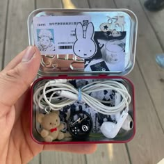 someone is holding an open tin box with various items in it, including earbuds