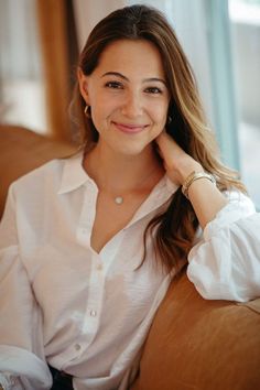 a woman sitting on top of a brown couch next to a glass window and smiling at the camera