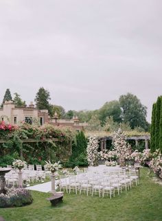 an outdoor wedding venue with white chairs and flowers on the lawn, surrounded by greenery