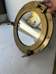 a hand holding a porthole mirror on the side of a wall