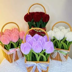 three baskets filled with flowers sitting on top of a white cloth covered table next to each other