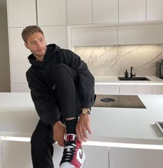 a man sitting on top of a kitchen counter next to a white refrigerator freezer