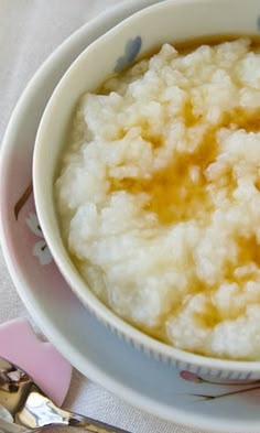 a white bowl filled with rice on top of a pink and white table cloth next to silverware