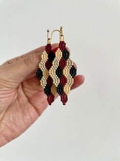 a hand holding a pair of beaded earrings in it's left hand, on a white background