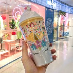 a person holding up a cup with sprinkles and an ice cream cone