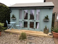 a small garden shed with patio furniture and potted plants on the decking area